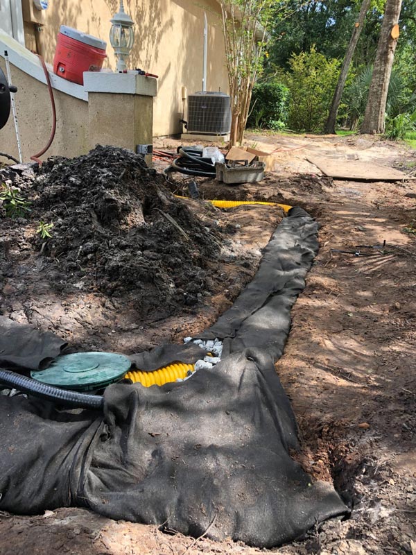Corrugated drain pipe set in filter fabric along a house