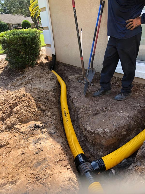 Yellow drain line routed from a downspout into a trench